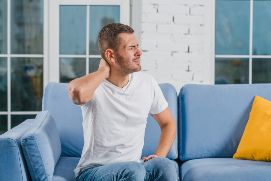 Handsome man sitting on cozy sofa suffering from painful neck